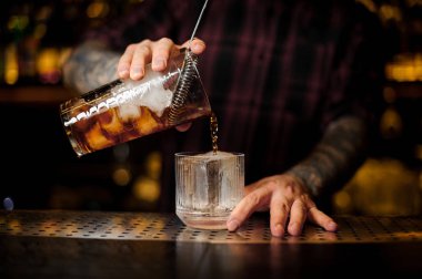 Bartender pouring a Old Fashioned cocktail from the measuring cup to a glass on the bar counter