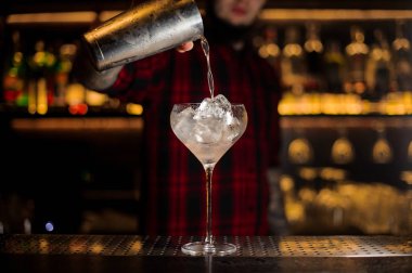 Barman pouring alcoholic drink into a glass with ice cubes