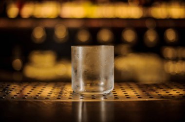 Small empty misted cocktail glass on the bar counter in the background of golden lights