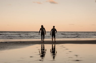 İki genç erkek siyah wetsuits alacakaranlıkta denize yürüme kurulları ile yürüme fiziksel olarak uygun