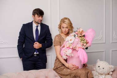 Erkeğini yakınındaki çiçek kutusu ile kanepede oturan bej elbiseli kız