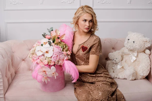 Chica en el vestido beige sentado en el sofá con la caja de flores — Foto de Stock
