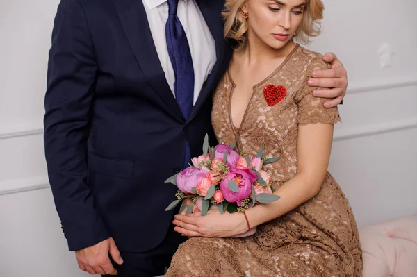 Man hugging a girl in the beige dress sitting on the couch with the box of flowers — Zdjęcie stockowe