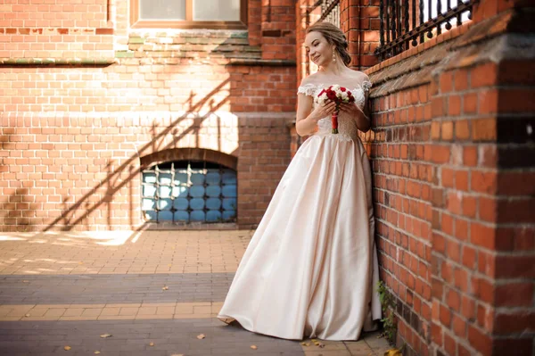 Piękna panna młoda w sukni ślubnej biały stojący w pobliżu ściany z czerwonej cegły — Zdjęcie stockowe