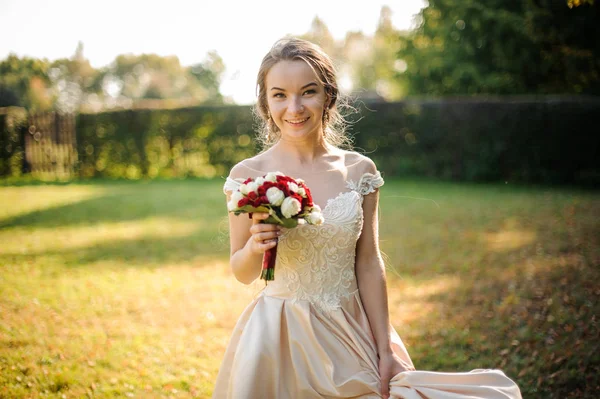 Novia sonriente en un vestido de novia blanco sosteniendo un ramo de rosas rojas beauriful — Foto de Stock