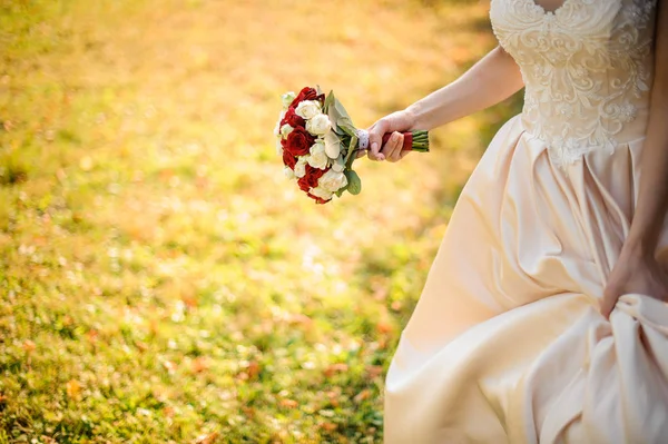 Noiva em um vestido de noiva branco correndo com um lindo buquê de rosas vermelhas — Fotografia de Stock