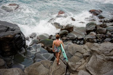 Arka görünümü kadın Multi mayo duran kayaların üzerinde sörf ile renkli