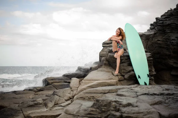 Menina desportiva no maiô multi colorido sentado perto do surf na rocha — Fotografia de Stock