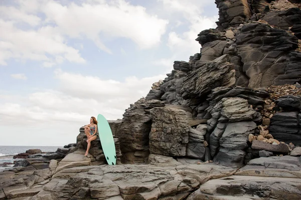 Belle fille sexy dans le maillot de bain multicolore assis près du surf sur le rocher — Photo