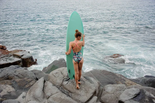 Visão traseira menina desportiva no maiô multi colorido em pé na praia de rock — Fotografia de Stock
