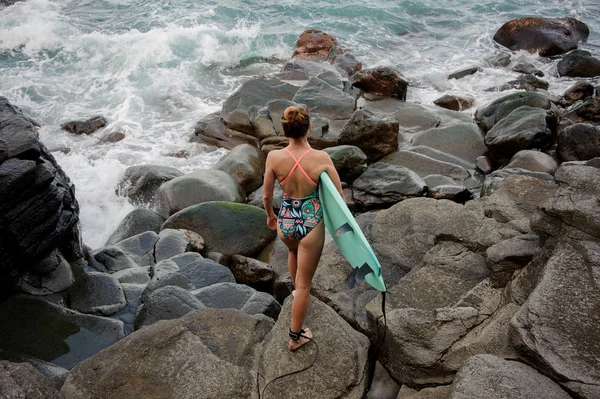 Mädchen im mehrfarbigen Badeanzug, das mit der Brandung auf den Felsen spaziert — Stockfoto