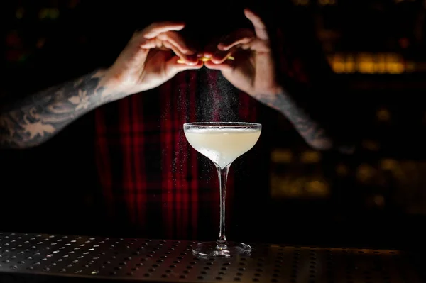 バーテンダー バーで暗闇の中で光とおいしいアルコール飲料とオレンジの皮の汁をエレガントなカクテル グラスを散水 — ストック写真