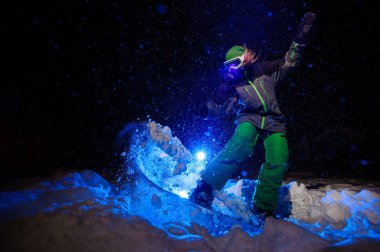 Dağ yamacında atlama yeşil bir spor giyim giymiş aktif kadın snowboard