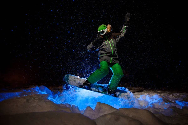 Mujer snowboarder vestida con una ropa deportiva verde saltando en la ladera de la montaña — Foto de Stock