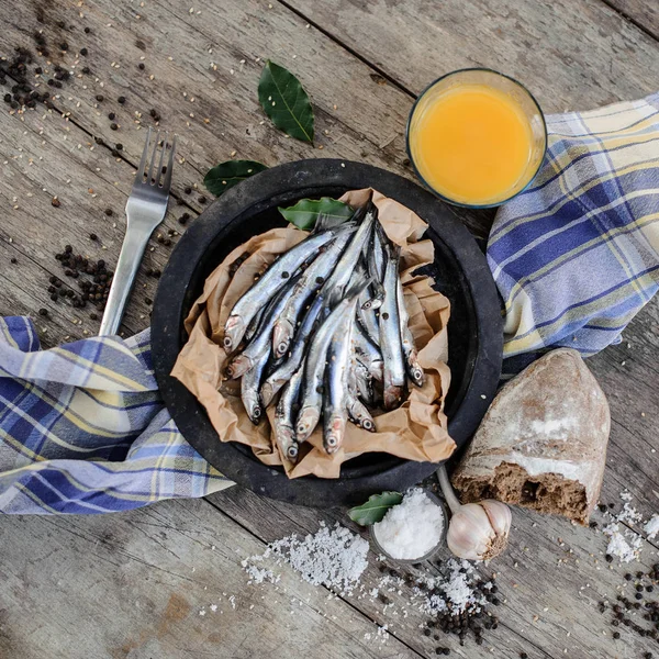 Las anchoas frescas en el plato con en un papel de hornear con una comida alrededor en la servilleta azul cerca de la horquilla — Foto de Stock