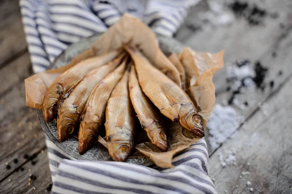 Delicioso pescado secado al humo en un plato sobre un papel de hornear en la servilleta de rayas grises — Foto de Stock