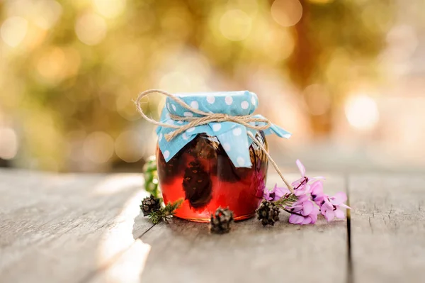 Zapfen-Marmelade im Glas mit blauer Stoffmütze und daneben rosa Blüten auf dem Tisch — Stockfoto