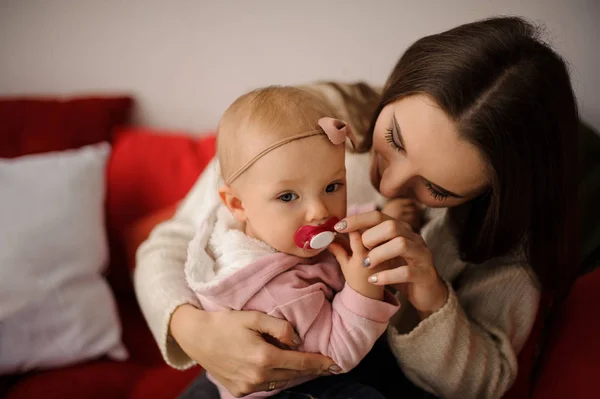 Woman holding her cute little daughter on hands and help her with a babys dummy — Stock Photo, Image