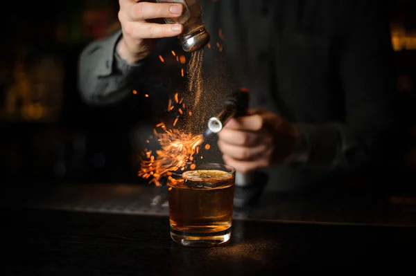 Bartender adding to a cocktail cinnamon and flaming it — Stock Photo, Image