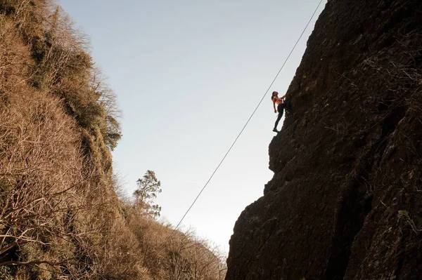 見上げると傾斜した岩の上を登るロープ装備の女の子 — ストック写真