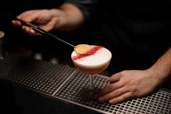 Professioneller Barkeeper, der mit einer Pinzette ein köstliches Cocktail-Dekor der getrockneten Limettenscheibe ergänzt — Stockfoto