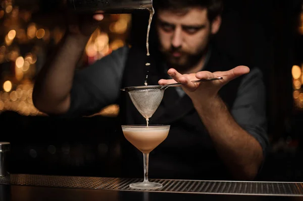 Просессиональная брюнетка-бармен наливает коктейль из шейкера через фильтр — стоковое фото