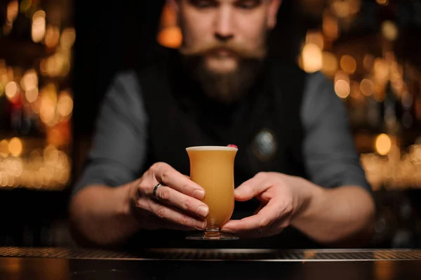Barman avec une barbe servant un cocktail dans le verre avec de la mousse décorée d'un bouton de rose rouge — Photo