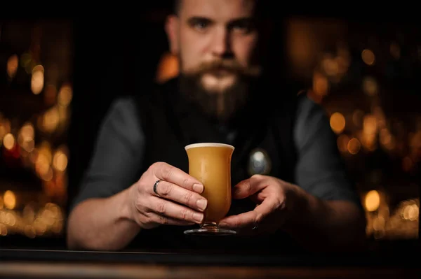 Barman professionnel avec une barbe servant un cocktail dans le verre avec de la mousse décorée d'un bouton de rose rouge — Photo