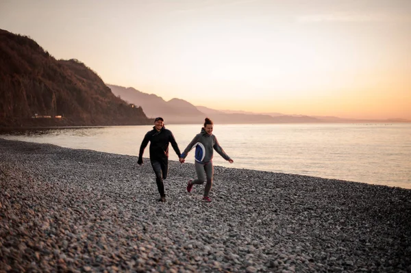 Молода пара біжить на пляжі тримаючись за руки — стокове фото