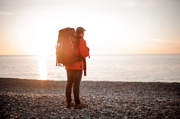 Hombre con una mochila de pie y mirando al mar —  Fotos de Stock