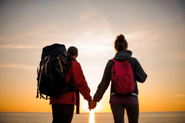 Pareja con mochilas de pie y mirando al mar al atardecer —  Fotos de Stock