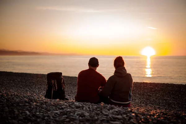 Par med rygg säckar som sitter på stranden och tittar på havet — Stockfoto