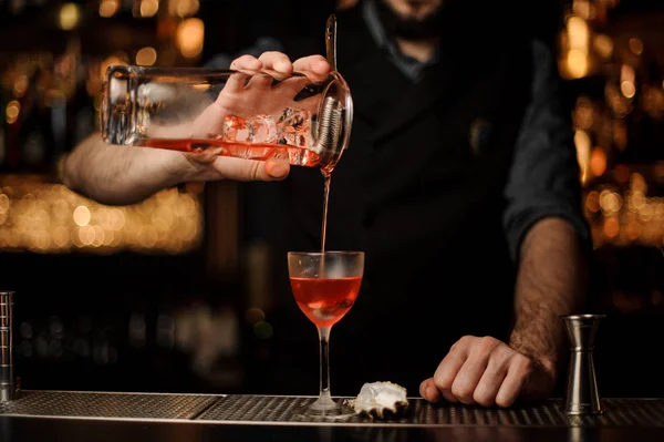 Barman verser un délicieux cocktail rouge de la tasse en verre de mesure à travers la passoire — Photo