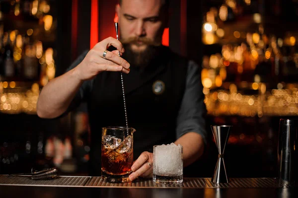 Barman revolviendo un delicioso cóctel marrón con una cuchara de acero en la taza de vidrio medidor — Foto de Stock