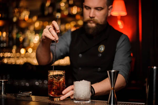 Barman revolviendo un delicioso cóctel con una cuchara de acero en la taza de vidrio medidor en el soporte de la barra — Foto de Stock