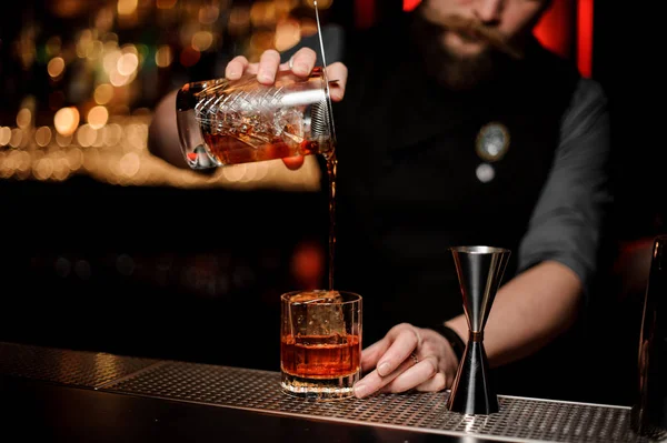 Barman masculin versant un cocktail de la tasse en verre de mesure à travers la passoire — Photo