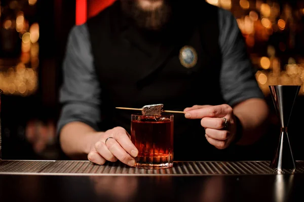 Cantinero masculino profesional que añade una pieza de brownie en el pincho con azúcar en polvo a una copa de cóctel — Foto de Stock