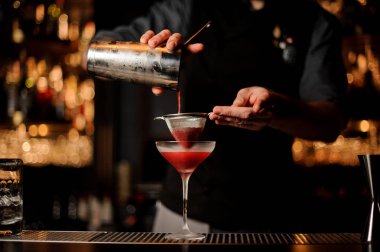 Profesyonel barmen cam için elek aracılığıyla pembe bir kokteyl dökme