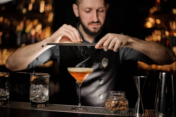 Barman masculin ajoutant à un cocktail dans le verre une noix de muscade râpée — Photo