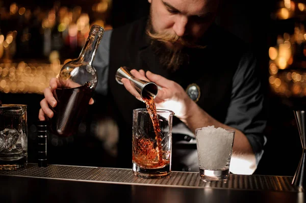 Barman nalije hnědý alkohol do koktejlu z ocelového skládáku — Stock fotografie