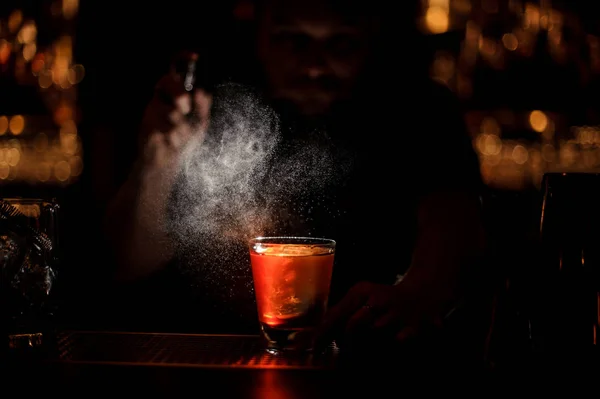 Cantinero profesional rociando a la copa de cóctel con un gran cubo de hielo en la oscuridad — Foto de Stock