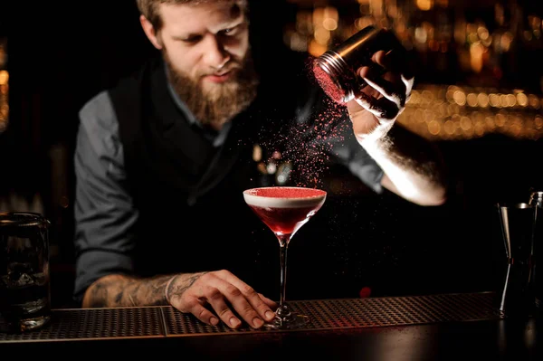 Barman profissional com uma barba acrescentando a um coquetel com um chantilly um pó vermelho — Fotografia de Stock