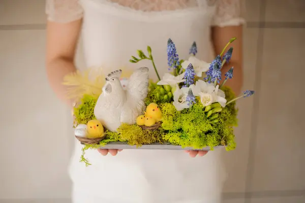Mädchen hält eine schöne Frühlingskomposition mit Spielzeug Chiken und weißen und blauen Blumen — Stockfoto