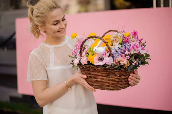 Menina sorridente segurando uma cesta de flores amarelas e rosa decoradas com coelhinho de brinquedo — Fotografia de Stock