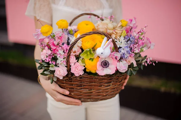 Girl holding a basket of yellow and pink flowers decorated with little toy bunny — Stock Photo, Image