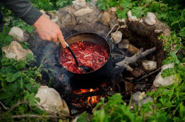Adam kamp ateşi üzerinde tencerede yahni kıpırdanırken