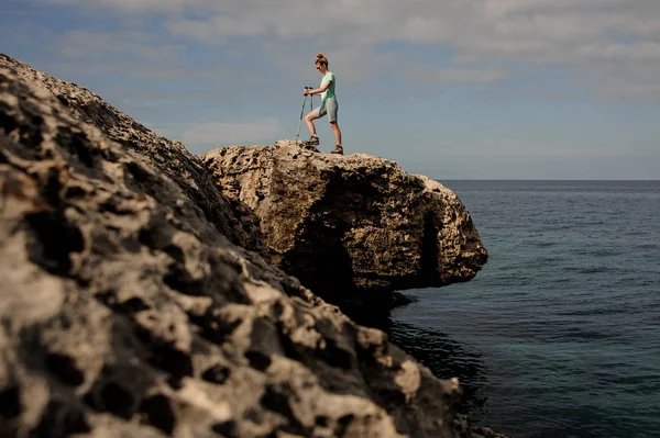 Ung flicka som går med pinnar på stenarna nära havet — Stockfoto