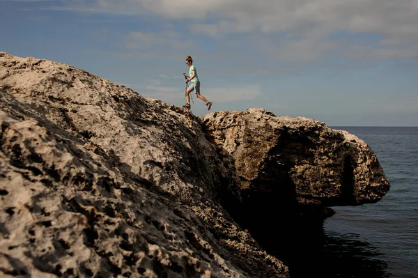 Ung kvinna som går med pinnar på stenig strand — Stockfoto