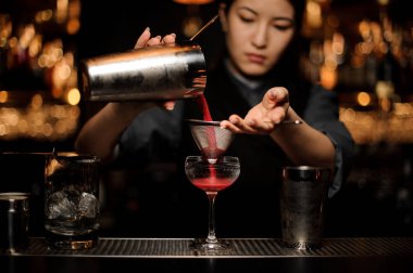 Shaker ve elek ile kokteyl döken kadın barmen