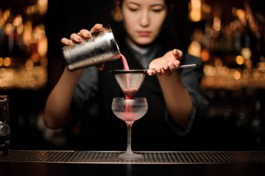 Kadın barmen shaker ve elek ile alkol kokteyl hazırlanıyor